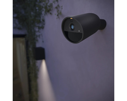 Une caméra de surveillance Philips Hue noire sans fil pour l''extérieur est fixée à un mur.