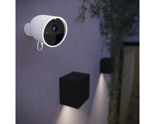 Une caméra de surveillance Hue est montée sur un mur, à côté de laquelle se trouvent deux lampes d''extérieur cubiques