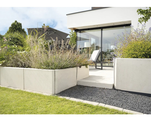 Jardin moderne avec parterres de plantes surélevés en béton, terrasse avec mobilier de jardin et parasol