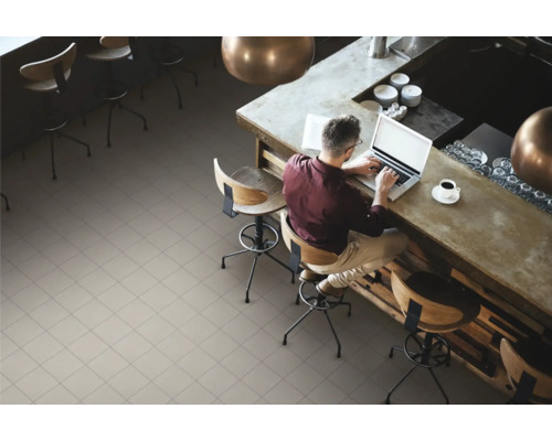 Heller, gefliester Boden in einem Café mit einem Mann, der an einem Tresen mit Laptop sitzt.