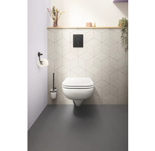 Salle de bains moderne avec WC suspendu, plaque de commande, brosse de toilette et support papier toilette.