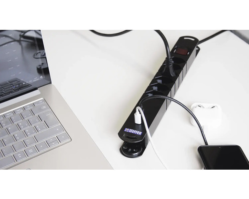 Steckdosenleiste mit angeschlossenen elektronischen Geräten auf einem Tisch.