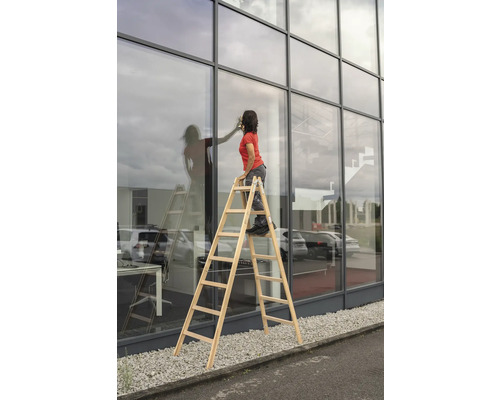 Femme sur un escabeau en bois nettoyant les vitres d''un bâtiment avec une façade en verre