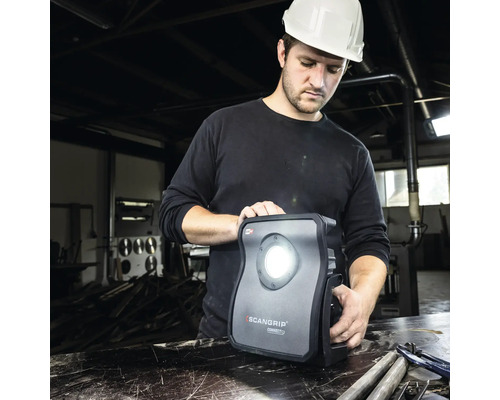 Un ouvrier avec un casque de protection utilise une lampe de travail Scangrip.