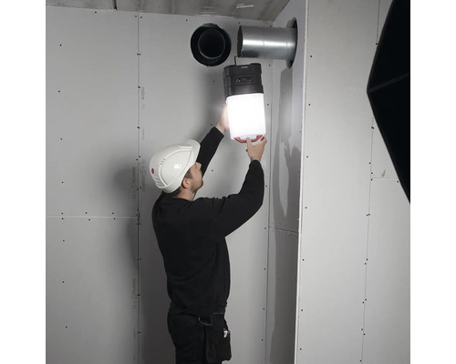 Un homme avec un casque fixe une lampe de chantier à un mur.