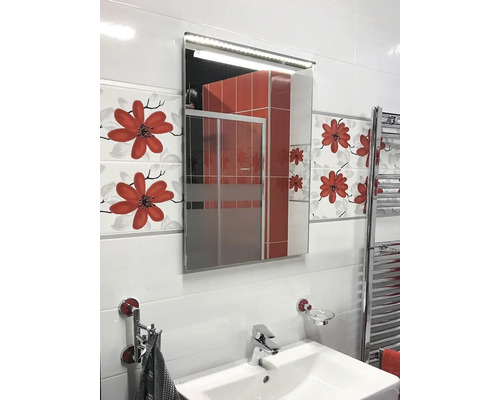 Salle de bain lumineuse avec lavabo, armoire de toilette éclairée et carrelage à motifs floraux