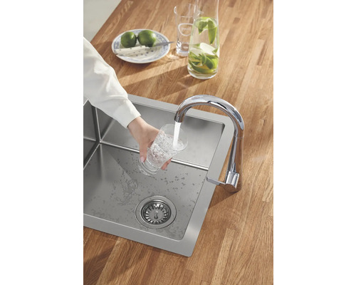 Évier en acier inoxydable avec robinet, sur une table en bois, une personne remplit un verre d''eau