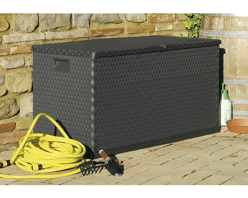 Aufnahme einer schwarzen Aufbewahrungsbox aus Kunststoff mit Gartenutensilien vor einer Steinmauer.