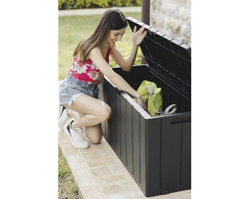 Frau öffnet eine Gartenbox zur Aufbewahrung von Gartengeräten im Aussenbereich.