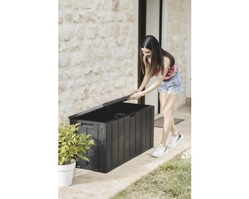 Frau öffnet eine schwarze Gartenbox zur Aufbewahrung im Außenbereich
