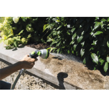 Scène de jardin avec une personne utilisant un arroseur de jardin pour nettoyer un mur.