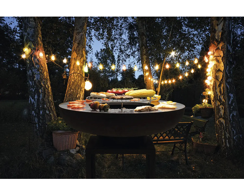 Outdoor-Szene mit Kugelgrill, Speisen, Baumstämmen und Lichterketten
