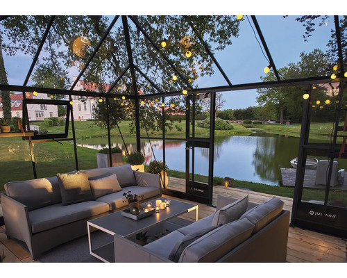 Serre avec coin salon, table et éclairage donnant sur un lac