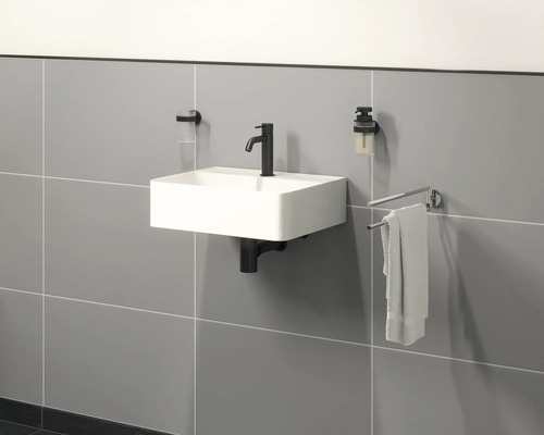 Hängewaschbecken mit Armatur, Seifenspender, Zahnputzbecher und Handtuchhalter an einer Wand