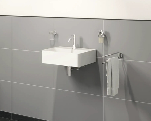 Wandwaschbecken mit Armatur, Seifenspender, Handtuch und Zahnputzbecher in einem Badezimmer