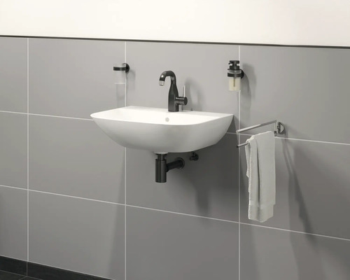 Lavabo mural avec robinetterie, distributeur de savon et porte-serviettes devant un mur carrelé