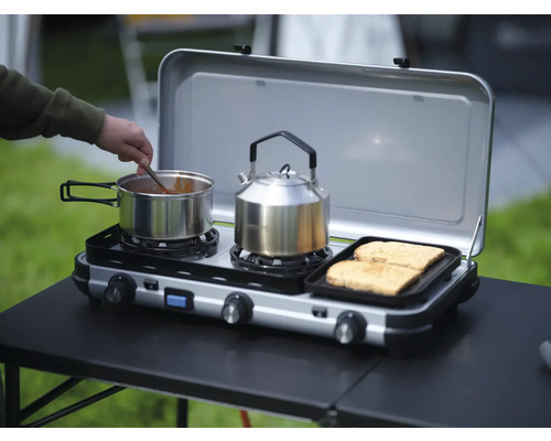 Campingkocher mit Kochtopf, Teekessel und Toastbrot auf einem Tisch im Freien
