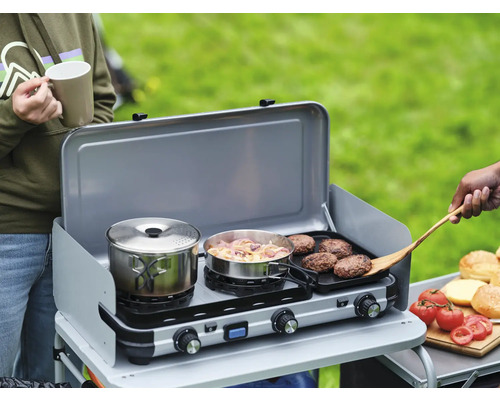 Campingkocher mit Topf, Pfanne, Burger, Tomaten und Brötchen im Freien