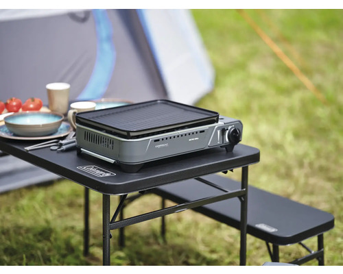 Table de camping avec réchaud à gaz, vaisselle et nourriture à l''extérieur