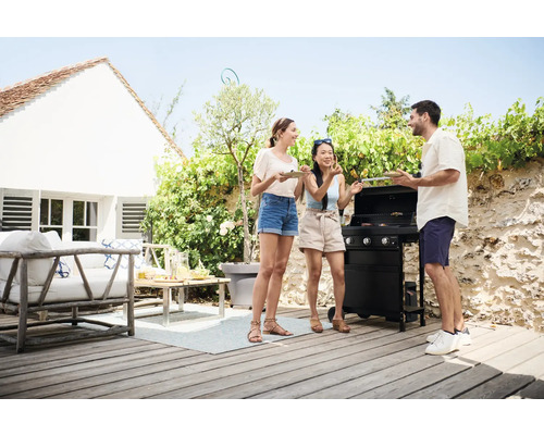 Scène d''extérieur avec trois personnes à un espace barbecue avec barbecue et mobilier de jardin