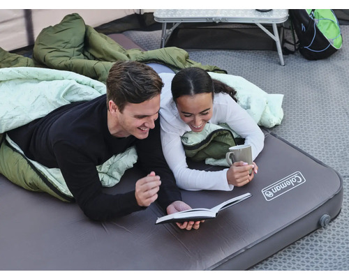 Ein Paar entspannt im Zelt auf einer Coleman Luftmatratze und liest ein Buch
