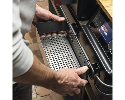 Eine Person setzt einen perforierten Behälter aus Metall in einen Grill ein.