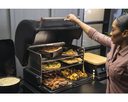 Femme ouvrant un grill avec plusieurs niveaux remplis de nourriture.