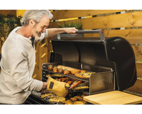 Un homme fait griller des légumes et de la viande sur un barbecue d''extérieur.