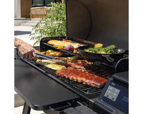 Ein Grill mit Rippchen, Fisch und Gemüse wird mit einer Zange gewendet.