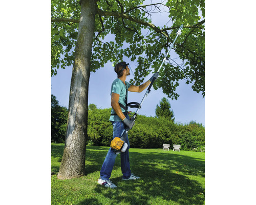 Homme avec protection faciale et débroussailleuse coupant un arbre dans le jardin.