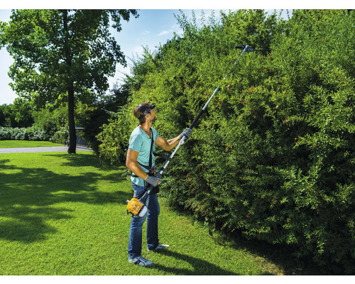 Une personne taille une haie avec un taille-haie.