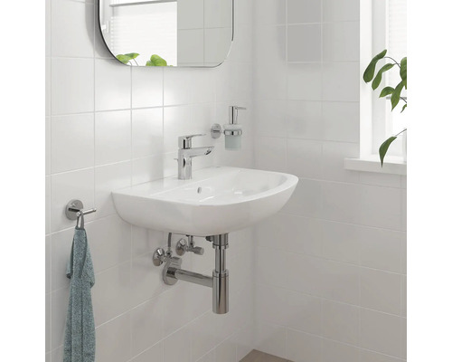 Lavabo de salle de bains avec robinet, miroir, distributeur de savon et porte-serviettes sur un mur carrelé.