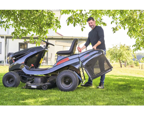 Un homme fixe un bac de ramassage sur une tondeuse autoportée dans le jardin.