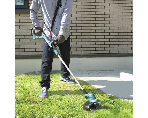 Une personne utilise un coupe-bordures à batterie dans le jardin pour couper l''herbe.