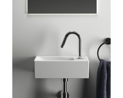 Detailaufnahme eines kleinen, rechteckigen Waschbeckens mit Armatur und Handtuchring in einem Badezimmer.