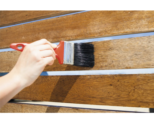 Une personne applique une lasure pour bois sur une terrasse en bois avec un pinceau.