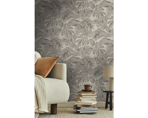 Salon avec papier peint imprimé de feuilles, canapé, pile de livres et lampe.