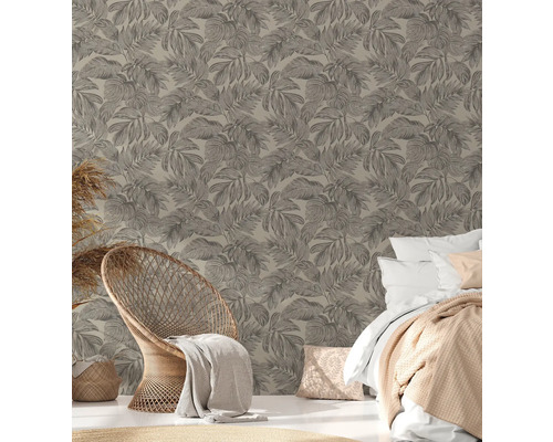 Une chambre avec un mur à motifs de feuilles, un fauteuil en rotin et un lit.