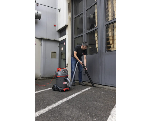 Un homme nettoie le sol devant une porte de garage avec un aspirateur eau et poussière.