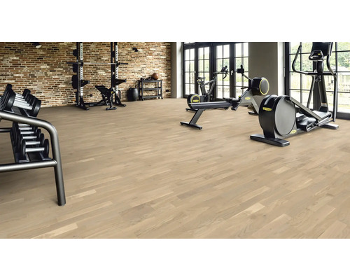 Salle de sport avec plancher en bois, haltères et appareils d'entraînement.