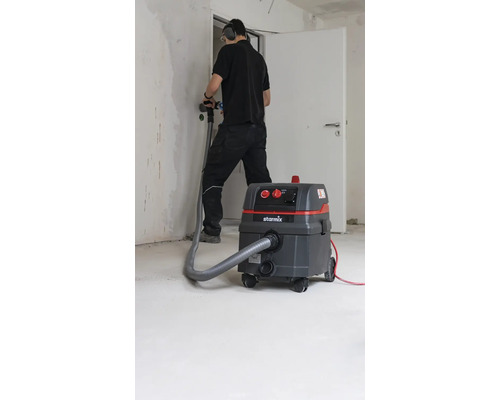 Artisan avec aspirateur industriel lors de travaux de rénovation dans une pièce.