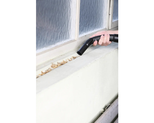 Une personne aspire les feuilles d''un cadre de fenêtre avec un aspirateur