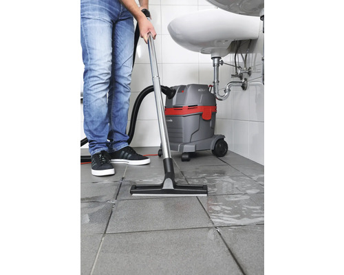 Une personne utilise un aspirateur eau et poussière dans la salle de bain pour nettoyer le carrelage.