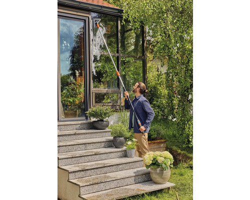 Mann reinigt Fenster eines Wintergartens mit Fensterwischer und Teleskopstiel.