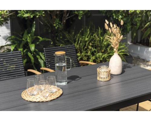 Gartenszene mit Tisch, Stühlen, Gläsern, Wasserkaraffe, Kerze und Dekoration.