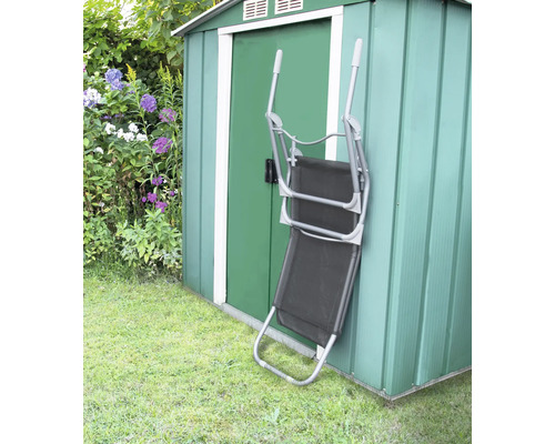 Chaise longue pliante en métal et textile appuyée contre un cabanon de jardin vert.