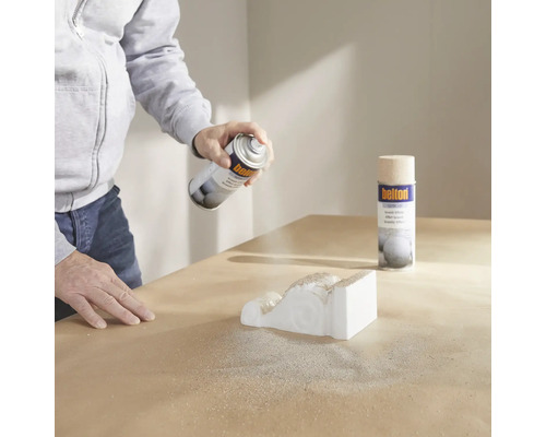 Une personne vaporise une moulure décorative avec un spray de structure.