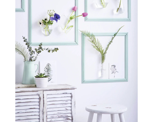 Dekorative Wandgestaltung mit Blumen in Vasen, die in Rahmen an einer Wand hängen, und einem Sideboard mit Pflanzen.