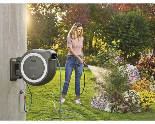 Femme arrosant des fleurs avec un dévidoir mural dans le jardin