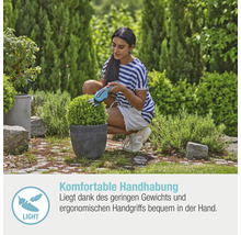 Eine Frau schneidet mit einer Akku-Strauchschere einen Buchsbaum im Garten.